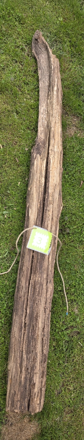 GedankenGuss - Holzskulpturen und abstrakten Kunstwerken -Eine kleine, hellgrüne und weiße Zierfahne mit einer Zahl hängt an einem dicken Seil über einem verwitterten Holzbrett, das auf einem Stück grünem Gras liegt.