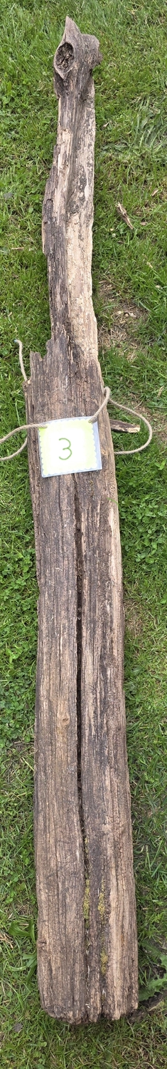 GedankenGuss - Holzskulpturen und abstrakten Kunstwerken -Eine kleine, hellgrüne und weiße Zierfahne mit einer Zahl hängt an einem dicken Seil über einem verwitterten Holzbrett, das auf einem Stück grünem Gras liegt.