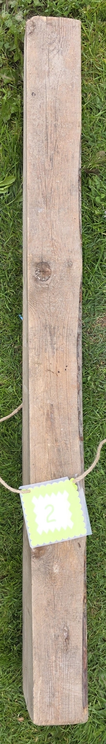 GedankenGuss - Holzskulpturen und abstrakten Kunstwerken -Eine kleine, hellgrüne und weiße Zierfahne mit einer Zahl hängt an einem dicken Seil über einem verwitterten Holzbrett, das auf einem Stück grünem Gras liegt.
