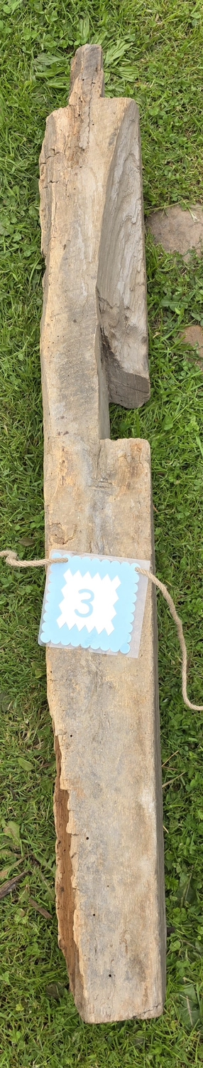 GedankenGuss - Holzskulpturen und abstrakten Kunstwerken -Eine kleine Blau und weiße Zierfahne mit einer Zahl hängt an einem dicken Seil über einem verwitterten Holzbrett, das auf einem Stück grünem Gras liegt.
