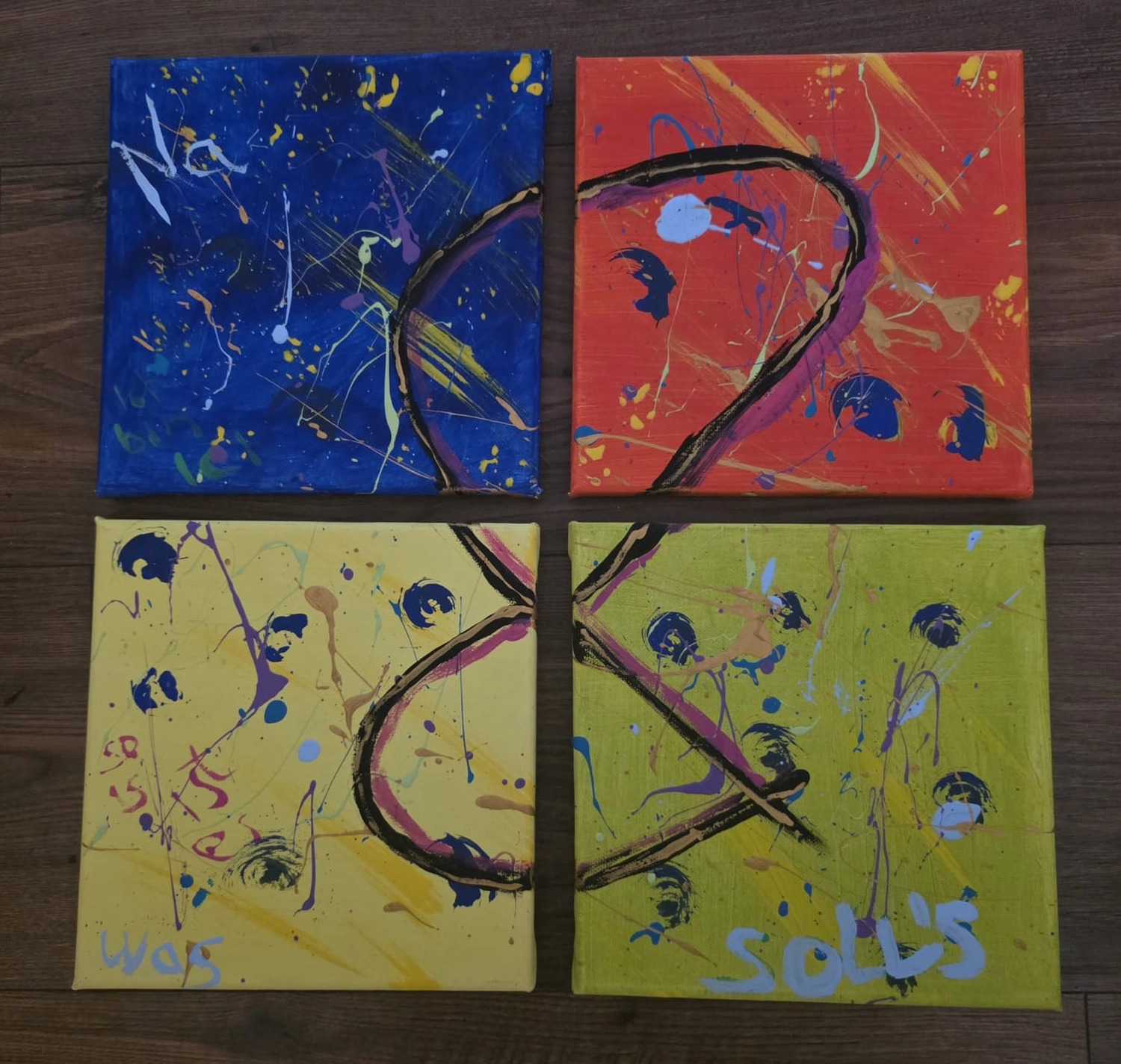 GedankenGuss - Holzskulpturen und abstrakten Kunstwerken -  Vier quadratische Leinwandbilder, angeordnet in einem Raster, zeigen abstrakte Farbspritzer und Buchstaben auf blauem, rotem, gelbem und grünem Hintergrund.